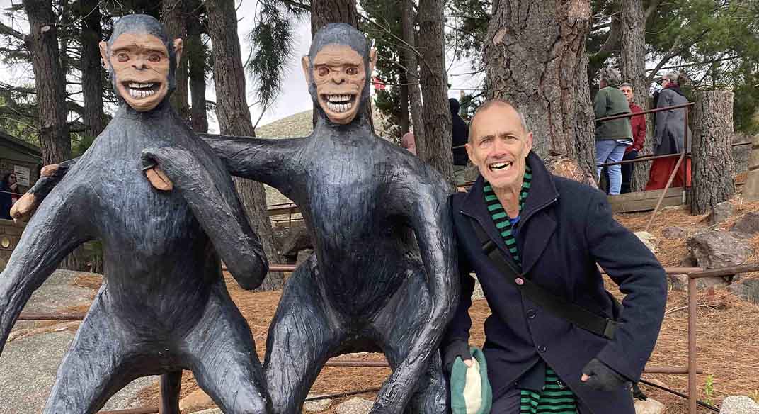 Andy next to two statues of monkeys in a park. Andy is pulling a funny face.